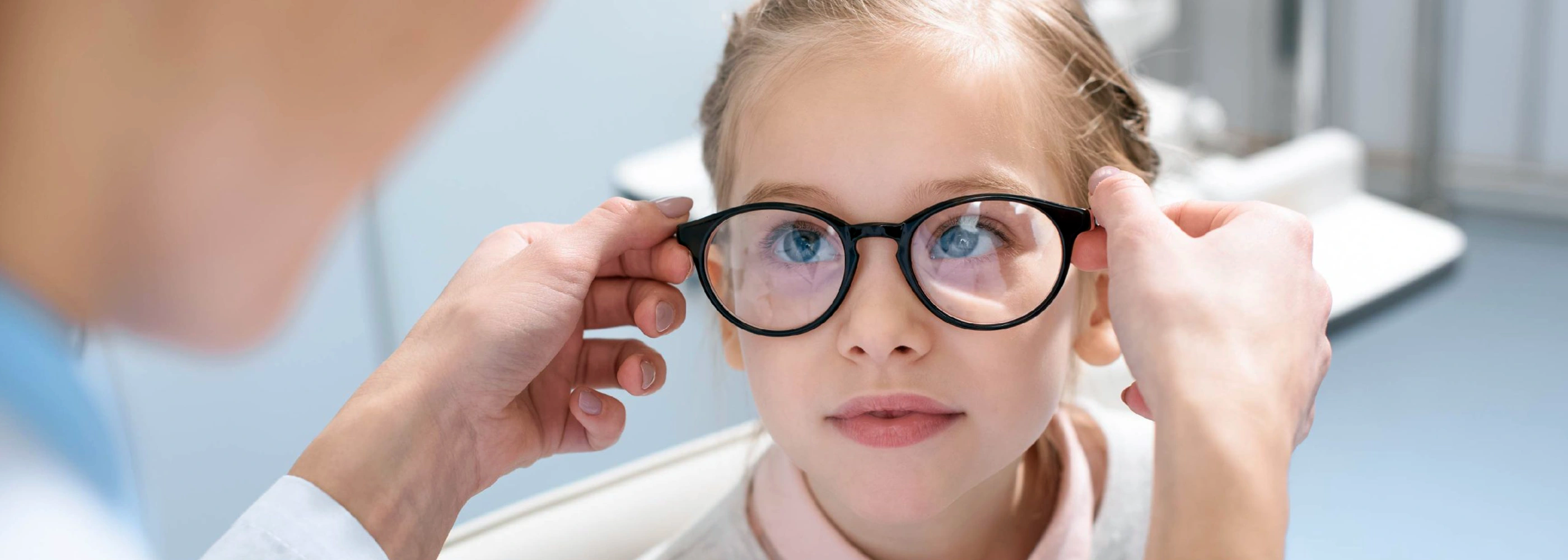 Een close-up van een jong meisje met blond haar dat een nieuwe bril aangemeten krijgt door de kinderoogarts